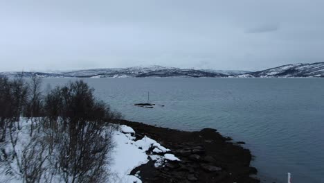 Drohnenansicht-In-Tromsø,-Die-Von-Einem-Verschneiten-Gebiet-Mit-Bergen-Voller-Schnee-Im-Winter-In-Norwegen-Zum-Meer-Fliegt