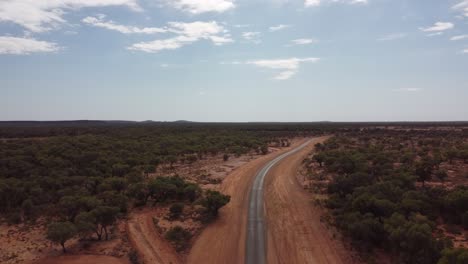 Drone-Ascendiendo-Sobre-Una-Carretera-Rural-Muy-Remota-Rodeada-De-Tierra-Roja-Y-árboles-En-El-Interior-De-Australia