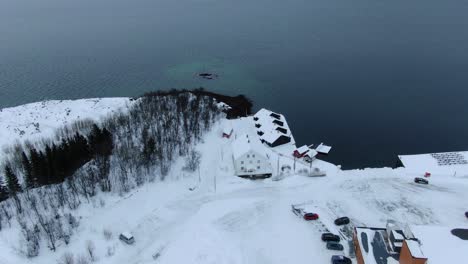 Drone-view-in-Tromso-area-flying-over-Finnsnes-in-winter-and-showing-the-sea-next-to-the-snowy-town-with-a-hotel-in-Norway
