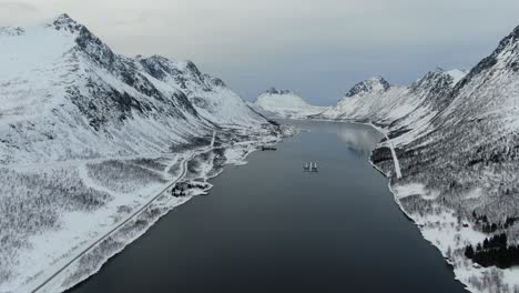 Drone-view-in-Tromso-area-in-winter-flying-over-a-fjord-surrounded-by-white-mountains-in-Norway
