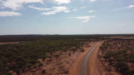 Drone-Volando-Sobre-Una-Carretera-Rural-Muy-Remota-Rodeada-De-Tierra-Roja-Y-árboles-En-El-Interior-De-Australia