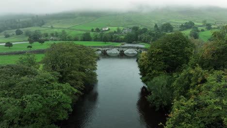 Fast-wide-tracking-down-through-trees-and-over-bridge-in-Yorkshire-Dales,-United-Kingdom