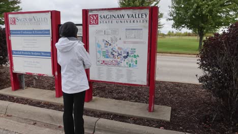 Woman-looking-at-a-map-on-the-campus-of-Saginaw-Valley-State-University-in-University-Center,-Michigan-with-gimbal-video-walking-behind