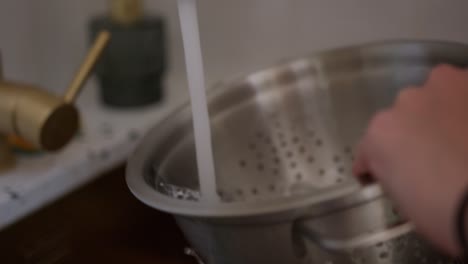 Person-washing-steel-strainer-sieve-metal-bowl-in-sink,-close-up