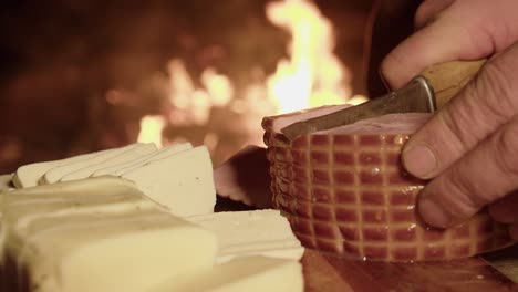 Cured-ham-is-cut-into-thick-slices-on-board-near-flaming-hot-camp-fire
