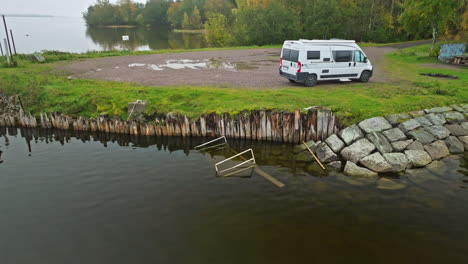 Weißer-Lieferwagen,-Der-Am-Ruhigen-Seeufer-Mit-Herbstbäumen-Im-Hintergrund-In-Schweden-Geparkt-Ist