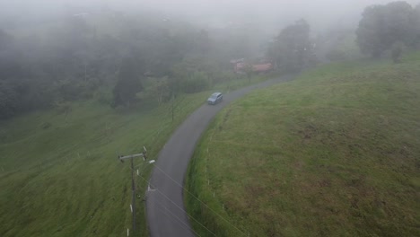 driving-through-mountains-in-modern-SUV-car,-aerial-video,-drone,-driving-in-foggy-mountain-with-cows
