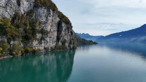 A-stunning-turquoise-lake-at-the-foot-of-a-steep-cliff-with-beautiful-blue-hazy-mountains-in-the-distance