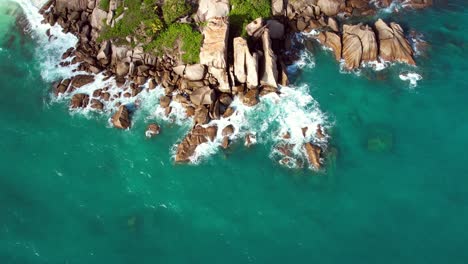 Bird-eye-drone-shot-of-north-east-point-beach,-huge-rock-boulders-waves-crushing-on-and-turquoise-water,-Mahe-Seychelles-60-fps