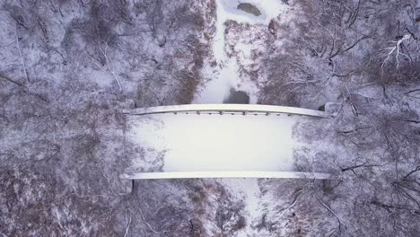 Bird's-eye-view-of-snowy,-abandoned-highway-bridge-over-frozen-river
