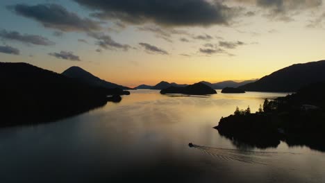 Aerial-view-of-small-boat-traveling-through-golden-sunlight-and-silhouetted-peninsulas-in-Elaine-bay-in-Pelorus-Sound-Te-Hoiere-of-Marlborough-Sounds,-South-Island-of-New-Zealand-Aotearoa