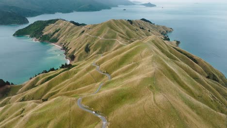 Scenic-aerial-view-of-sloping-peninsula-landscape-at-Te-Aumiti-French-Pass-with-campervan-traveling-along-winding-road-in-Marlborough-Sounds,-South-Island-of-New-Zealand-Aotearoa