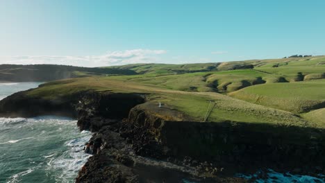 Reverse-aerial-drone-view-of-Slope-Point-lighthouse-overlooking-rough-and-wild-ocean-and-rugged-coastline-in-the-Catlins-region-of-the-South-Island-of-New-Zealand-Aotearoa