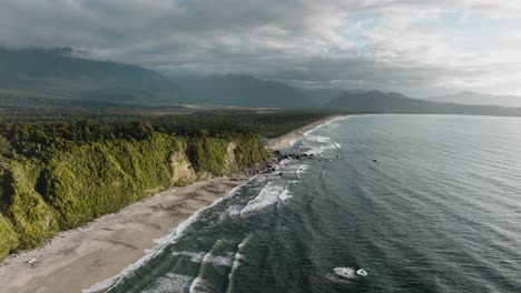 Aerial-view-of-vast,-dramatic-and-remote-wilderness-landscape-of-trees-and-mountains-with-Tasman-Sea-in-Bruce-Bay,-South-Westland,-New-Zealand-Aotearoa