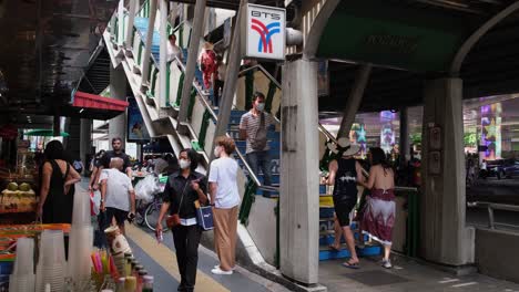 Commuters,-daily-wage-workers,-and-tourists-walking-along-the-busy-sidewalk-of-Sukhumvit-road-near-Phrom-Phong-BTS-train-station,-with-street-food-vendors-on-the-sides,-in-Bangkok,-Thailand