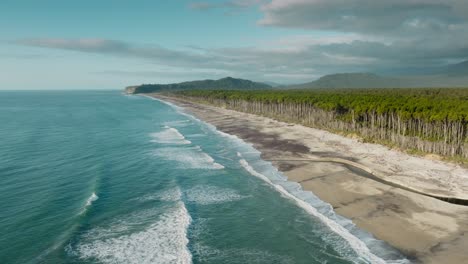 Aerial-view-of-vast,-wild,-rugged-and-remote-landscape-of-Bruce-Bay-with-sandy-beach,-forest-of-native-rimu-trees,-and-mountains-in-the-distance,-South-Westland,-New-Zealand-Aotearoa