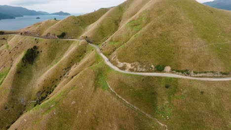Stunning-aerial-view-of-campervan-traveling-along-remote,-mountainous-road-towards-Te-Aumiti-French-Pass-in-Marlborough-Sounds,-South-Island-of-New-Zealand-Aotearoa