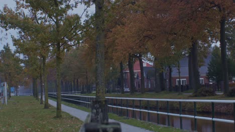 european-park-in-the-village-of-Netherlands-Holland-in-the-fall-autumn-with-houses,-trees-and-water-canal-next-to-the-quiet-street-road