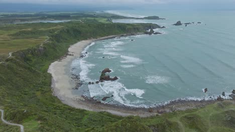 Aerial-landscape-view-of-Tasman-Sea-and-waves-rolling-into-shoreline-in-the-remote-wilderness-of-Cape-Foulwind-on-West-Coast,-South-Island-of-New-Zealand-Aotearoa