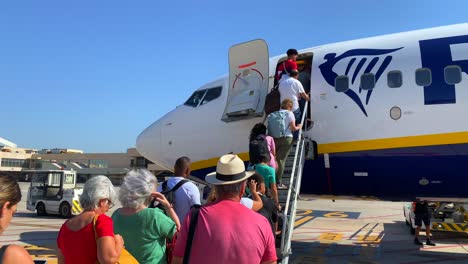 People-standing-and-slowly-boarding-a-big-Ryanair-boeing-airplane-in-Malaga-international-airport-on-a-sunny-day-in-Spain,-summer-holiday-vacation-time,-4K-static-shot