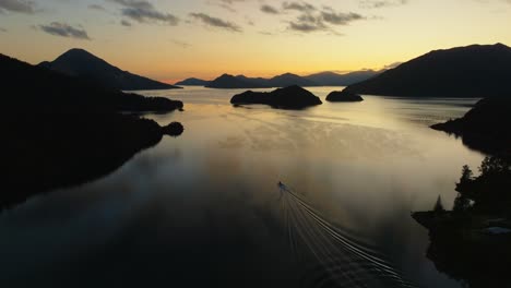 Aerial-view-of-golden-sunrise-with-boat-traveling-through-placid,-calm-waters-in-the-Pelorus-Sound-Te-Hoiere-in-the-Marlborough-Sounds,-South-Island-of-New-Zealand-Aotearoa