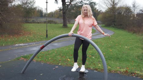 Athletic-blonde-haired-woman-performs-balance-exercise-outdoors