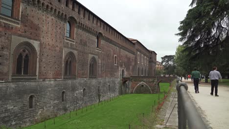 Verteidigungsgraben-Des-Schlosses-Sforzesco-Mit-Steinbrücke-Im-Hintergrund-Und-Menschen,-Die-Herumlaufen