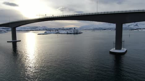 Vista-De-Drones-En-La-Zona-De-Tromso-En-Invierno-Volando-Junto-A-Un-Puente-Que-Conecta-Dos-Islas-Llenas-De-Nieve-Sobre-El-Mar-En-Noruega