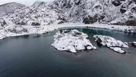 Vista-De-Drones-En-La-Zona-De-Tromso-En-Invierno-Volando-En-Círculos-Sobre-Una-Pequeña-Isla-Con-Nieve-Conectada-Con-Un-Puente-Colgante-De-Madera-En-Noruega