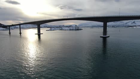 Vista-De-Drones-En-La-Zona-De-Tromso-En-Invierno-Volando-Junto-A-Un-Puente-Que-Conecta-Dos-Islas-Llenas-De-Nieve-Sobre-El-Mar-En-Noruega