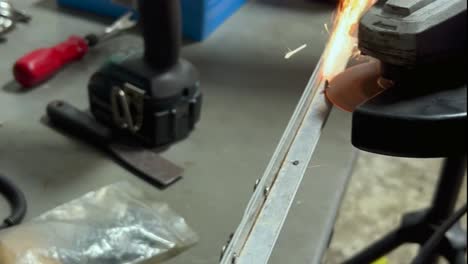 A-close-up-of-a-person-using-a-powered-metal-saw-to-cut-a-screw,-causing-orange-sparks-to-fly