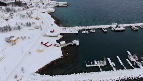 Drohnenansicht-In-Der-Gegend-Von-Tromsø-Im-Winter-über-Einer-Verschneiten-Landschaft,-Umgeben-Vom-Meer-Und-Einem-Gefrorenen-Hafen-Mit-Booten-Und-Weißen-Bergen-In-Norwegen