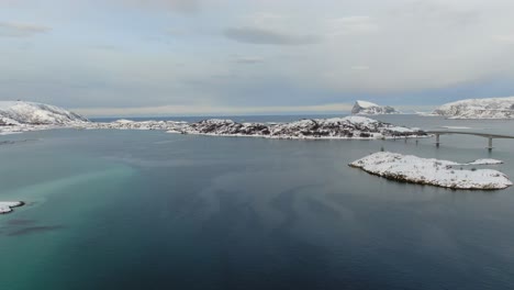 Drone-view-in-Tromso-area-in-winter-flying-over-snowy-islands-next-a-bridge-connecting-white-islands-in-Norway