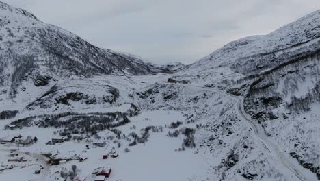 Drohnenansicht-In-Der-Gegend-Von-Tromsø-Im-Winter,-Die-über-Eine-Verschneite-Landschaft-Mit-Holzhäusern-Und-Weißen-Bergen-In-Norwegen-Fliegt