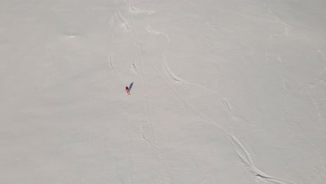 Aerial-top-down-shot-of-skier-skiing-downhill-snowy-mountains-with-curves-in-sun---Having-fun-on-icy-Norwegian-mountain