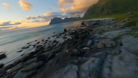 Speed-flight-over-coastline-of-Lofoten-with-rocks-in-water-and-green-mountain-slope-at-golden-sunset---Forward-drone-movement