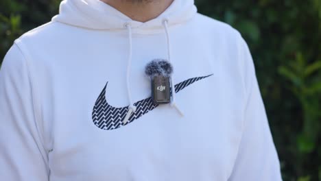 Hand-Turning-On-DJI-MIC-Attached-To-White-Sports-Hoody-With-Deadcat-On-Top