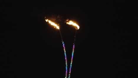 Zwei-Antennen-Mit-Roten-Flammenspitzen-Erhellen-Die-Nacht,-Während-Mehrfarbige-Regenbogen-Neonlichtröhren-Ihre-Dünnen-Rahmen-Erhellen