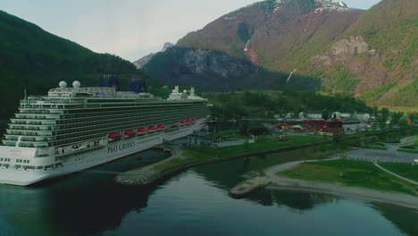 Aerial-drone-forward-moving-shot-over-cruise-ship-docked-at-the-port-of-Flam-surrounded-by-mountains-in-Central-Norway-during-morning-time