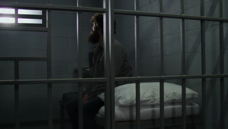 Krimineller-Sitzt-Auf-Dem-Bett-In-Der-Gefängniszelle-Und-Blickt-Auf-Das-Vergitterte-Fenster