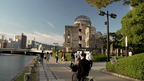 Besucher,-Die-Auf-Dem-Weg-Neben-Dem-Denkmal-Für-Die-Atombombenkuppel-In-Hiroshima-Neben-Dem-Fluss-Motoyasu-Spazieren