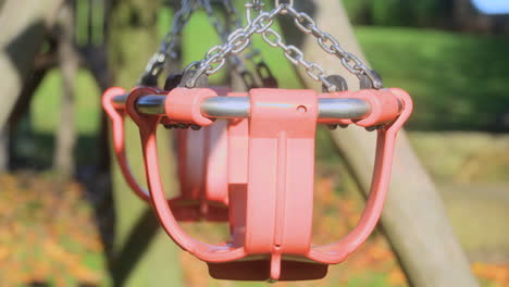 Empty-playground-swings-on-a-sunny-autumn-afternoon,-closer-crop-with-track-right