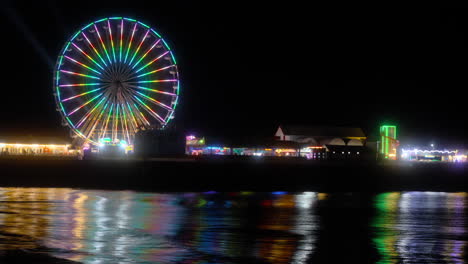 Big-wheel-ride-and-amusements,-at-night-with-lights-reflecting-off-the-incoming-tide-at-Central-Pier,-Blackpool,-Lancashire,-England,-UK