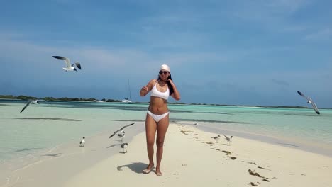 Latin-WOMAN-FEED-SEAGULLS,-birds-flying-around-on-white-sand-beach,-PHOTO-TRAVEL-MOMENT