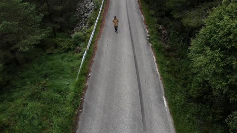Aerial-top-down-shot-of-person-walking-on-street-in-forest-landscape-of-Norway