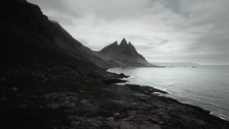 Aerial-vesturhorn-mountain,-black-sand-beach-stokksnes,-flying-over-volcanic-dark-moody-rocks,-moody-scenery,-Iceland