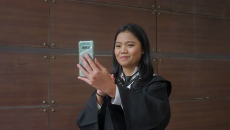 Chica-Asiática-Indonesia-Con-Videollamada-Con-Vestido-De-Graduación,-Agitando-Las-Manos,-Sonriendo,-Orgullosa