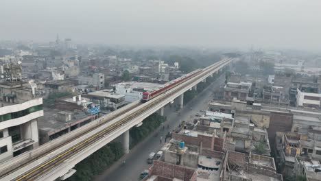 Aerial-View-Of-Orange-Line-Metro-Train-Near-McLeod-Road-In-Lahore-On-Elevated-Track-With-Hazy-Air-Pollution-In-Background