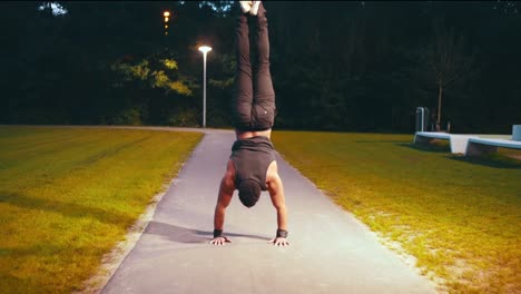 muscular-black-guy-does-handstand-push-up-on-the-middle-of-the-road-in-a-park-night-time