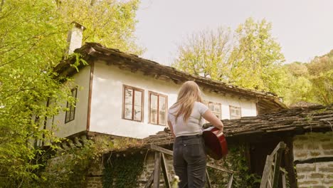 Beautiful-country-girl-strums-acoustic-guitar-rustic-village-scene